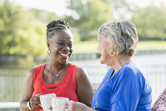 Two older women smiling and chatting over a cup of coffee