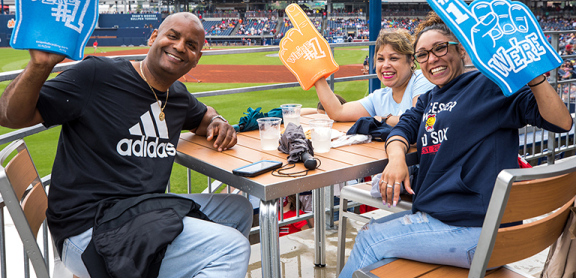 Three smiling Advocates staff members sitting at a table at a WooSox game. They each have a foam finger in Advocates orange and blue that says "We're number one."